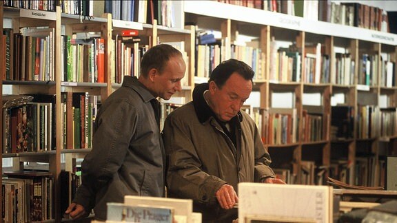 Zwei Männer stehen in einer Bibliothek und blättern in Büchern.