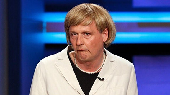 Hängende Mundwinkel und Perlenkette - Wer kann das wohl sein? Reiner Kröhnert als Angela Merkel.