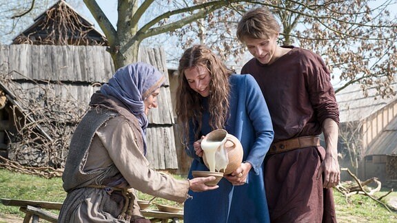 Jolanthe (Svenja Jung) und Veit von Hammerlitz (Merlin Rose) verteilen den süßen Brei an eine Dorfbewohnerin (Komparse).