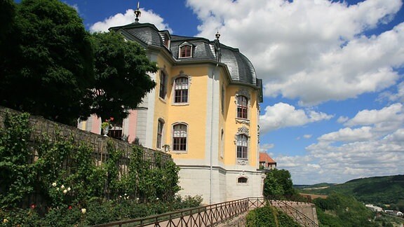 Blick auf ein Schloss, welches vor strahlend blauem Himmel auf einem begrünten Hügel thront