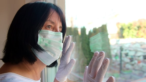 Eine Frau mit Mund-Nasen-Schutz sieht aus einem Fenster