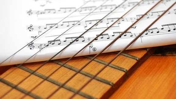 Ein Notenblatt ist unter die Saiten einer Gitarre gelegt