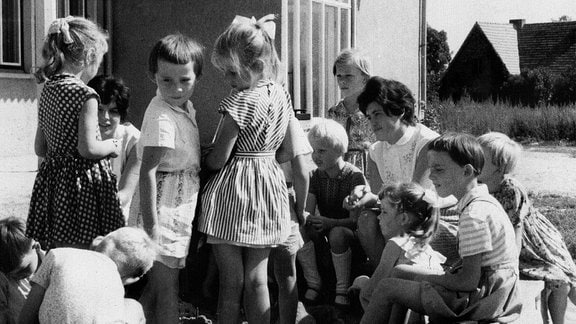 Schwarz-Weiß-Bild: Die "Kinder von Golzow" stehen um ihre Lehrerin in einem Sandkasten.