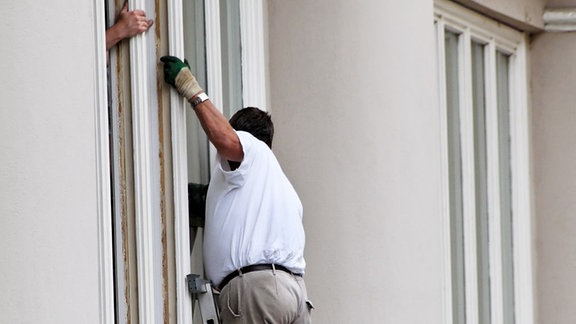 ein Bauarbeiter wechselt an einem Haus die Fenster aus