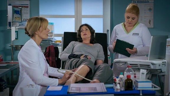 eine Ärtzin und eine Krankenschwester untersuchen eine liegende Frau am Bein