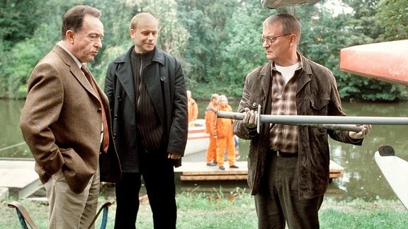 Der Kriminaltechniker Walter (Walter Nickel, rechts) zeigt den Kommissaren Ehrlicher (Peter Sodann, links) und Kain (Bernd Michael Lade, mitte) die vermutliche Tatwaffe.