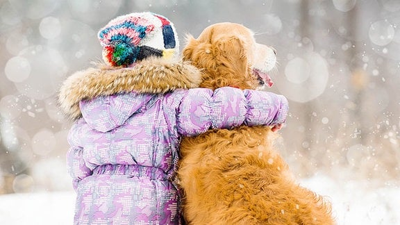 Ein kleines Mädchen und ein Hund sitzen im Schnee