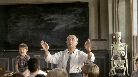 Clement Mathieu (Gerard Jugnot, hinen re.) dirigiert in einem Klassenzimmer.