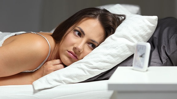 Eine schalflose Frau schaut auf Ihren Wecker nachts im Bett