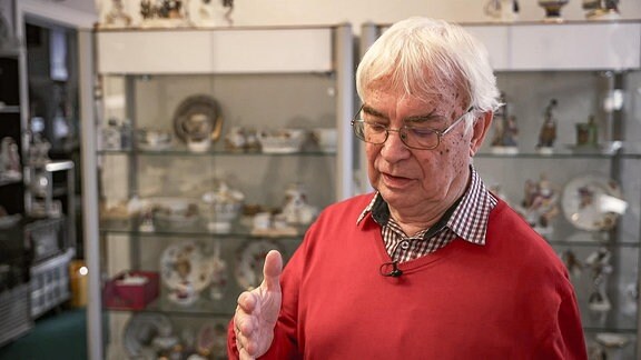 älterer Mann im roten Pullover in einem Antiquitätengeschäft