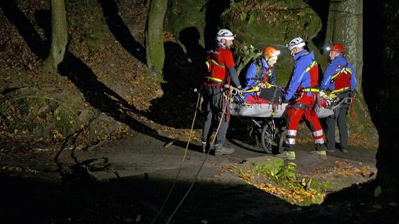 Eine Gruppe der Bergwacht transportiert einen Verletzten in einer Transporttrage auf einem Wagen über einen nächtlichen Waldweg.