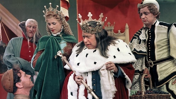 Prinzessin Liebreich (Gisela Kretzschmar), König Griesgram (Fred Kronström) und Prinz Eitel (Horst Drinda) blicken entsetzt auf einen lächelnden Mann herab.