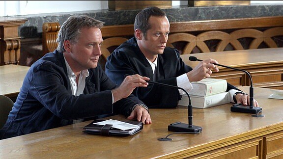 Zwei Männer sitzen auf der richterlichen Anklagebank.