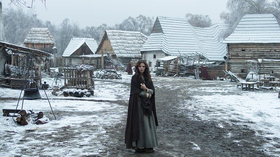 Eine junge Frau steht in einem verschneiten Dorf.