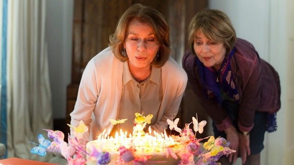 Zwei Frauen pusten Kerzen auf einer Torte aus.