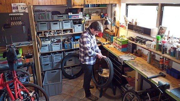 Eine Person steht in einer Werkstatt und arbeitet an einem Fahrradreifen. 