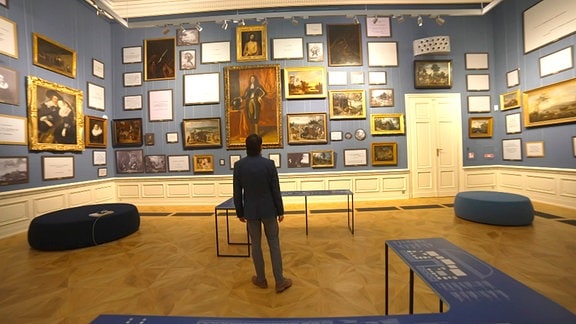 Im Herzoglichen Museum Gotha steht ein Mann vor einer Wand mit Gemälden.