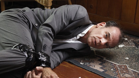 Herr Keppler (Martin Wuttke) liegt mit gefesselten Händen auf einem Fußboden.