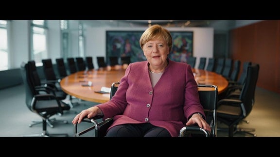 Angela Merkel sitzt auf einem Sessel im Bundeskanzleramt und schaut in die Kamera.