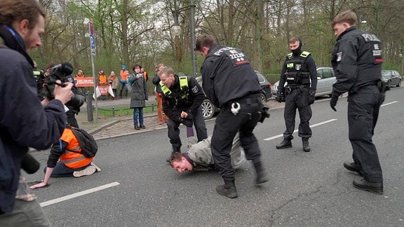 Der Klimaaktivist Lars Ritter wird unter Anwendung eines Schmerzgriffes von der Polizei von der Straße entfernt.