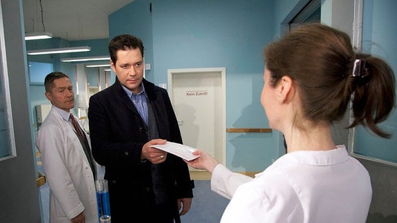 Dr. Brentano erhält von der Labor-Assistentin ein Untersuchungsergebnis. Dr. Kaminski betritt hinter ihm das Zimmer.