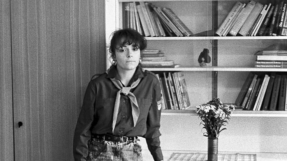 Kandidatin der 1. Leipziger Miss-Wahl, Mai 1989: Ramona March, in einem FDJ-Hemd und mit Halstuch eines Pionierleiters vor einer Anbauwand stehend.