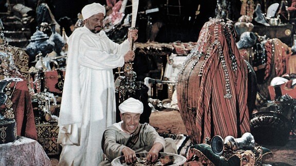 Cassim (Henri Vilbert, links) gönnt seinem einstigen Diener Ali Baba (Fernandel) den plötzlichen Reichtum nicht.