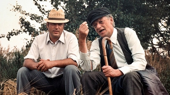 Zwei Männer sitzen an einem Feld und unterhalten sich.