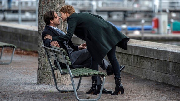 Jojo Hirt (Andrea Osvárt) küsst Johann Friedrich von Allmen (Heino Ferch), der auf einer Bank sitzt.