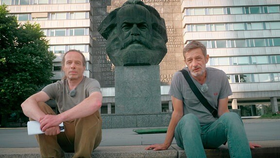 Zwei Männer sitzen vor der Karl-Marx-Statue in Chemnitz..
