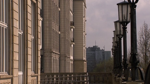 Blick zwishen Häuserwand und Laternen vorbei auf andere Gebäude einer Stadt.