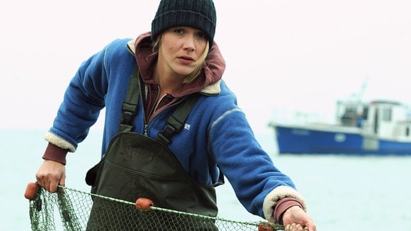 Eine Frau steht mit einen Fischernetz in einem Boot.