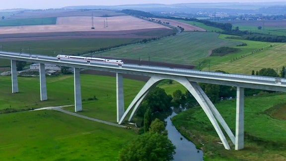 Eine schlanke Bogenbrücke führt über ein grünes Tal.