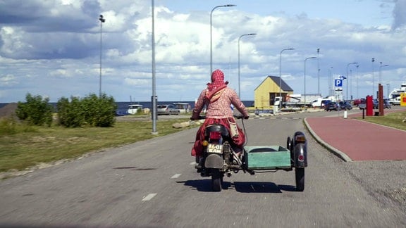 Eine Frau auf einem Motorrad mit Beiwagen fährt auf einer Küstenstraße.