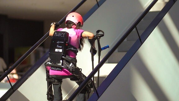 Eine Person mit einem roboterartigen Gestell am Körper, steigt eine Treppe hoch.