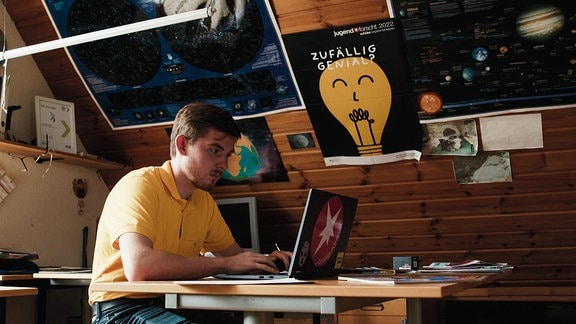 Ein Mann sitzt vor einem Laptop in einem Zimmer mit Dachschräge.
