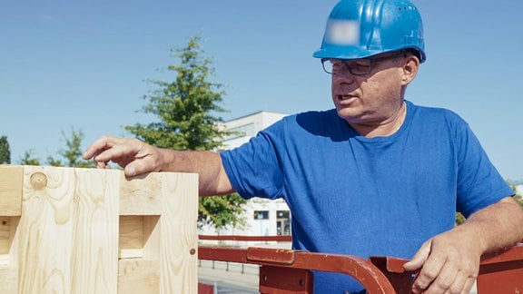 Ein Mann mit blauem Helm udn in blauem T-Shirt erklärt Holzbausteine.