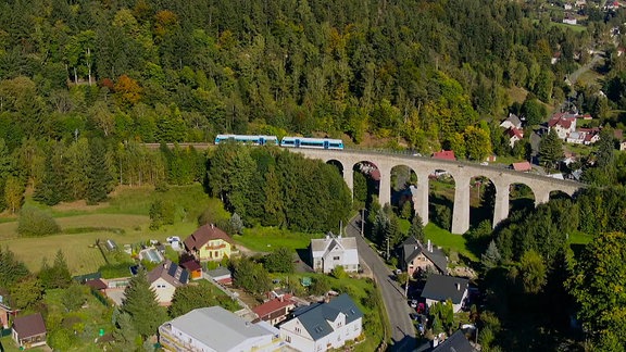Ein Viadukt, über das ein Zug durch ein grünes Tal fährt.