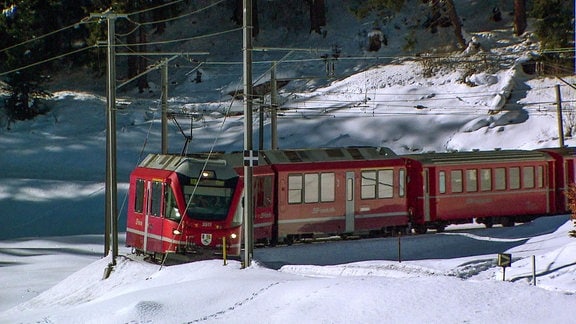Ein roter Zug fährt durch ein verschneites Tal.