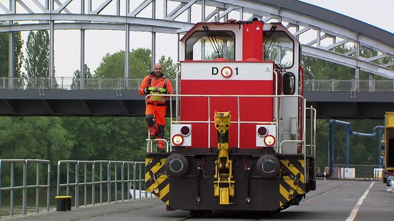 Ein Mann steht an der Führerkabine im Außenbereich einer roten Eisenbahn.