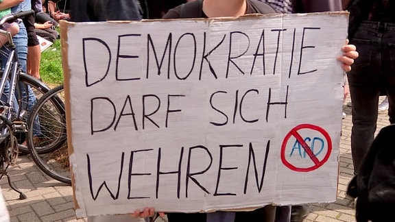 Ein Mensch hält ein großes Pappschild mit der Aufschrift "Demokratie darf sich wehren" und durchgestrichenem "AfD".