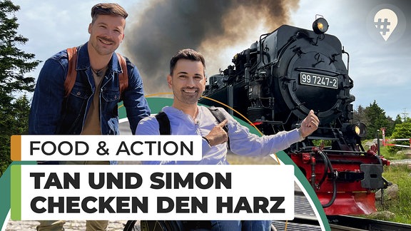 Zwei Männer vor einer Dampflokomotive, einer davon sitzt im Rollstuhl.