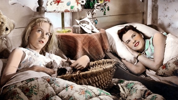 Zwei junge Frauen in Schlafkleidung liegen in nebeneinander stehenden Einzelbetten und schauen nachdenklich nach oben.