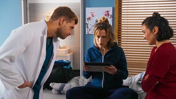 Ein Arzt und eine Ärztin zeigen einer erstaunen Patientin etwas auf einem Tablet.
