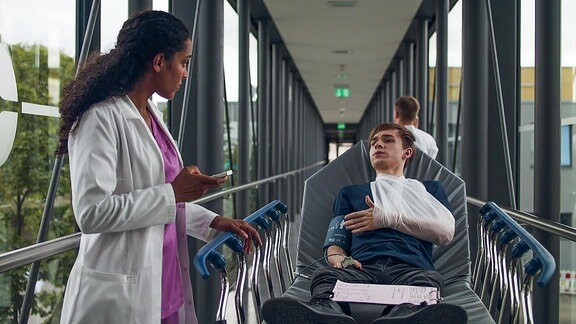 Eine Ärztin spricht mit einem jungen Mann, der auf einer Transportbett liegt.