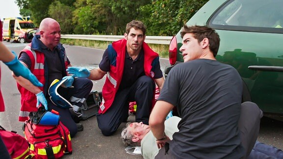 Ärzte und Sanitäter knien bei einer Verletzten, die auf einer Straße liegt. 