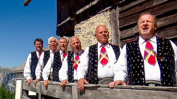 Sechs singende Männer auf einem Balkon.
