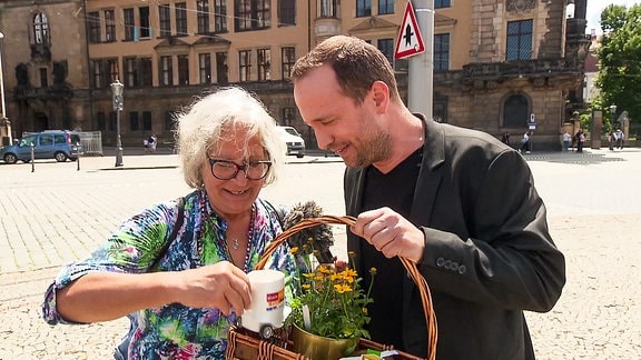 Ein Mann mit Mikrofon schaut mit einer Frau erfreut in einen Korb.