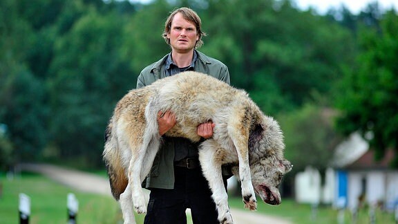 Waldner (Fabian Hinrichs) trägt den toten Wolf durch Kaskow.