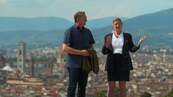 Axel Bulthaupt steht mit einer Frau vor einer Stadtkulisse, umgeben von Bergen.